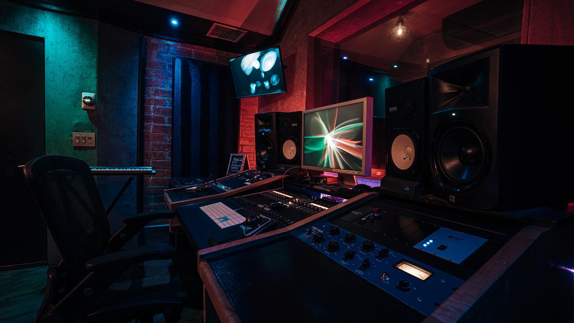 The Brick Room console and monitors under a red and teal wash on exposed brick